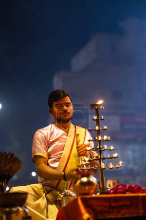 Foto de Varanasi, Uttar Pradesh, India - 03 de marzo de 2023: Ganga aarti, Retrato del joven sacerdote realizando pandillas del río santo aarti por la noche en dashashwamedh ghat con vestimenta tradicional con rituales hindúes - Imagen libre de derechos