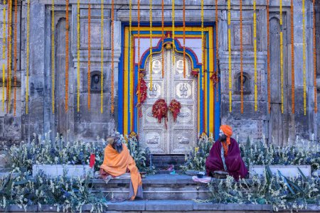 Photo for Kedarnath, Uttarakhand, India - October 15, 2022: Portrait of old naga sadhu baba in traditional dresses and ashes on faces sitting outside the holy temple of baba kedarnath. Temple door closed - Royalty Free Image