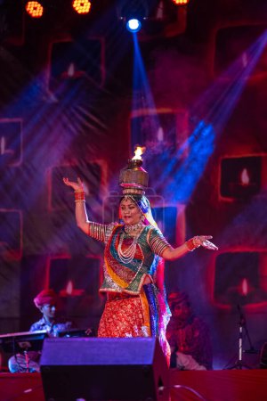 Photo for Pushkar, Rajasthan, India - November 05 2022: Female artist performing rajasthani folk dance Ghoomar in traditional colorful dress and metal pot with fire on head in Pushkar fair. Selective focus - Royalty Free Image