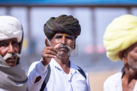 Téléchargez les photos : Pushkar, Rajasthan, Inde - 06 Novembre 2022 : Foire de Pushkar, Portrait d'un vieil homme rajasthani avec robe traditionnelle blanche et turban coloré jouissant au terrain de foire de pushkar - en image libre de droit