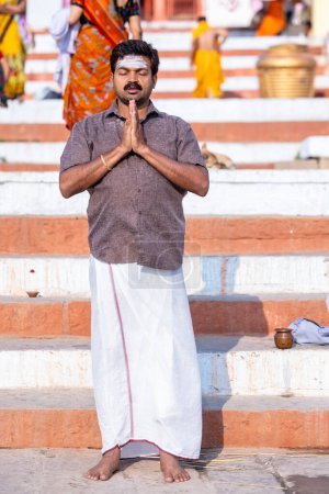 Téléchargez les photos : Varanasi, Uttar Pradesh, Inde - 05 mars 2023 : Portrait d'un saint homme brahmane du sud de l'Inde en costume traditionnel debout sur les ghats près de Ganges à Varanasi pour offrir la prière au seigneur soleil - en image libre de droit