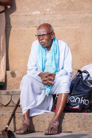 Téléchargez les photos : Varanasi, Uttar Pradesh, Inde - 05 mars 2023 : Portrait d'un vieil homme brahmane du sud de l'Inde en costume traditionnel assis sur les ghats près des anges à varanasi au lever du soleil - en image libre de droit