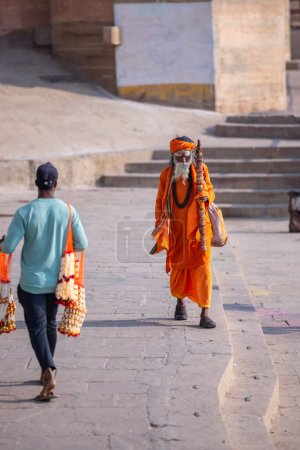 Téléchargez les photos : Varanasi, Uttar Pradesh, Inde - 05 mars 2023 : Portrait du saint sadhu baba en costume traditionnel marchant sur les ghats près des anges à varanasi - en image libre de droit