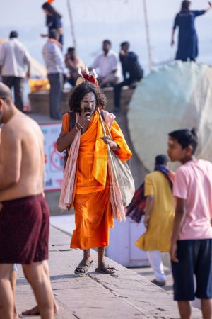 Foto de Varanasi, Uttar Pradesh, India - 05 de marzo de 2023: Retrato del santo sadhu baba en traje tradicional caminando sobre los ghats cerca de las pandillas en varanasi - Imagen libre de derechos