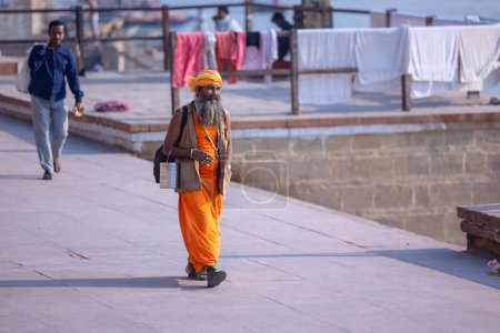 Téléchargez les photos : Varanasi, Uttar Pradesh, Inde - 05 mars 2023 : Portrait du saint sadhu baba en costume traditionnel marchant sur les ghats près des anges à varanasi - en image libre de droit