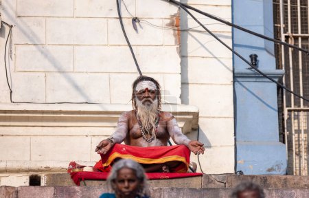 Photo for Varanasi, Uttar Pradesh, India - March 05 2023: Portrait of old holy sadhu baba in traditional dress sitting on ghats near ganges in varanasi. Kashi oldest and holy city - Royalty Free Image