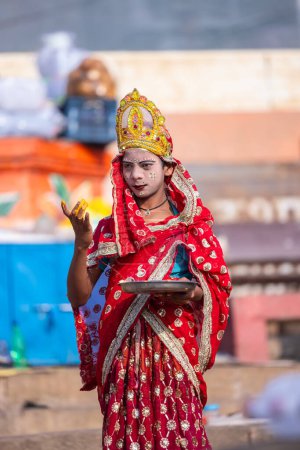 Photo for Varanasi, Uttar Pradesh, India - March 05 2023: Portrait of a young kid dress up like goddess parvati with painted face standing near on ghat near river ganges to make tilak on tourists - Royalty Free Image