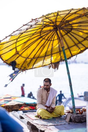 Foto de Varanasi, Uttar Pradesh, India - 05 de marzo de 2023: Retrato del sacerdote brahmán sagrado indio no identificado sentado en el ghat kedar cerca de las bandas fluviales en la ciudad de varanasi con ropa tradicional - Imagen libre de derechos