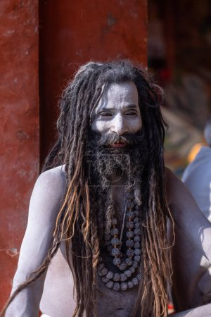 Téléchargez les photos : Varanasi, Uttar Pradesh, Inde - 05 mars 2023 : Portrait de vieux sadhu baba avec des cendres sur le visage et le corps assis sur le ghat de dashashwamedh près des anges à varanasi - en image libre de droit