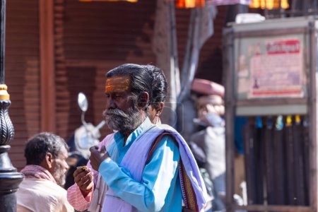 Téléchargez les photos : Varanasi, Uttar Pradesh, Inde - 05 mars 2023 : Portrait de vieux sadhu baba en costume traditionnel marchant sur des ghats près de Ganges à Varanasi. Kashi est la ville la plus ancienne et sainte - en image libre de droit