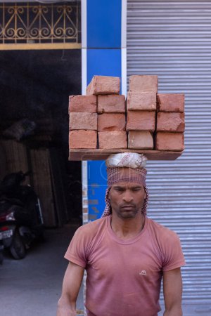 Téléchargez les photos : Varanasi, Uttar Pradesh, Inde - 05 mars 2023 : Rencontré au travail, main-d'œuvre masculine indienne travaillant sur le chantier de construction par la collecte des briques sur sa tête. - en image libre de droit