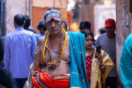 Foto de Varanasi, Uttar Pradesh, India - 05 de marzo de 2023: Retrato de un viejo sadhu baba sagrado con vestimenta tradicional caminando sobre ghats cerca de pandillas en varanasi. Kashi es la ciudad más antigua y santa - Imagen libre de derechos
