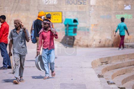 Téléchargez les photos : Varanasi, Uttar Pradesh, Inde - 05 mars 2023 : Rencontre au travail, Groupe de travailleurs indiens marchant sur des ghats près de ganga avec leur équipement sur le chantier de construction - en image libre de droit