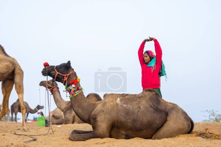 Foto de Retrato de una joven india rajasthani con colorido vestido tradicional llevando camello en Pushkar Camel Fair ground durante la mañana brumosa de invierno en Pushkar, Rajasthan. - Imagen libre de derechos