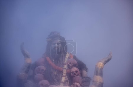 Foto de Masan Holi, Retrato de un artista masculino actuar como señor shiv con ceniza seca en la cara y el cuerpo también en el aire mientras se celebra el festival de holi como tradición en Harishchandra ghat en varanasi, India. - Imagen libre de derechos