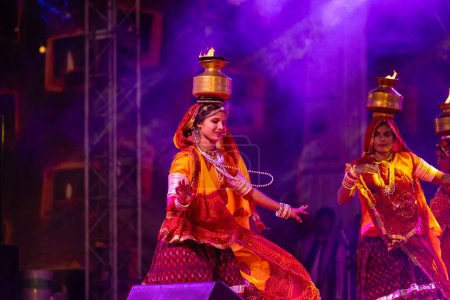 Téléchargez les photos : Pushkar, Rajasthan, Inde - 05 novembre 2022 : Une artiste féminine exécutant la danse folklorique rajasthani Ghoomar dans des robes colorées traditionnelles et des pots en métal avec feu à la foire de Pushkar. Concentration sélective. - en image libre de droit