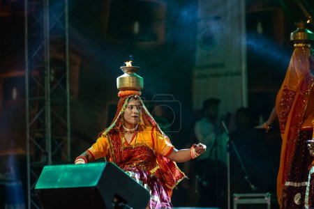 Foto de Pushkar, Rajastán, India - 05 de noviembre de 2022: Una artista femenina que realiza danza popular rajasthani Ghoomar en vestidos coloridos tradicionales y macetas de metal con fuego en la feria de Pushkar. Enfoque selectivo. - Imagen libre de derechos