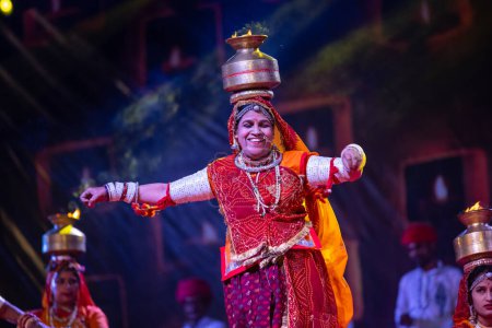 Foto de Pushkar, Rajastán, India - 05 de noviembre de 2022: Una artista femenina que realiza danza popular rajasthani Ghoomar en vestidos coloridos tradicionales y macetas de metal con fuego en la feria de Pushkar. Enfoque selectivo. - Imagen libre de derechos