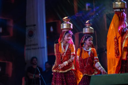 Foto de Pushkar, Rajastán, India - 05 de noviembre de 2022: Una artista femenina interpreta danza folclórica rajasthani Ghoomar en vestidos coloridos tradicionales y macetas de metal con fuego en la feria de Pushkar. Enfoque selectivo. - Imagen libre de derechos
