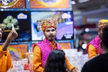 Foto de Nueva Delhi, India - 18 de noviembre de 2023: Retrato de un vendedor de ropa tradicional en un mostrador en la feria de Nueva Delhi para vender sus productos. - Imagen libre de derechos