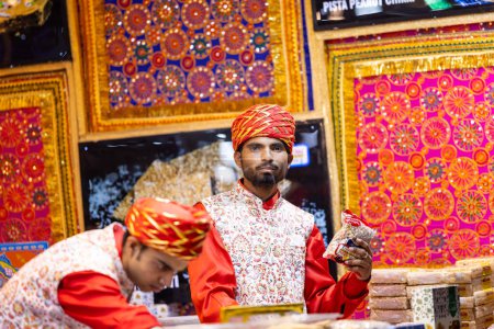 Téléchargez les photos : New Delhi, Inde - 18 novembre 2023 : Portrait d'un vendeur masculin en tenue traditionnelle à un comptoir du salon delhi pour vendre ses produits. - en image libre de droit