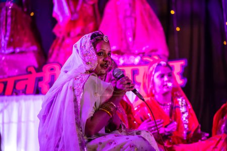 Foto de Bikaner, Rajastán, India - 13 de enero de 2023: Grupo de hermosas mujeres de ciclista en ropa tradicional rajashani colorida y realizando pooja gangaur cultural en el escenario durante el festival de camellos.. - Imagen libre de derechos
