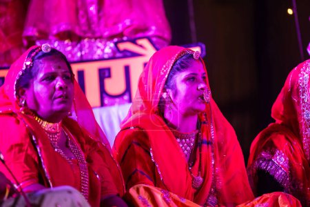 Foto de Bikaner, Rajastán, India - 13 de enero de 2023: Grupo de hermosas mujeres de ciclista en ropa tradicional rajashani colorida y realizando pooja gangaur cultural en el escenario durante el festival de camellos.. - Imagen libre de derechos