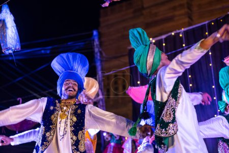 Foto de Bikaner, Rajastán, India - 13 de enero de 2023: Punjabi Bhangra, grupo de jóvenes sikh masculinos en el tradicional vestido colorido punjabi y turbante realizando danza bhangra con sonrisa en el festival del camello. - Imagen libre de derechos