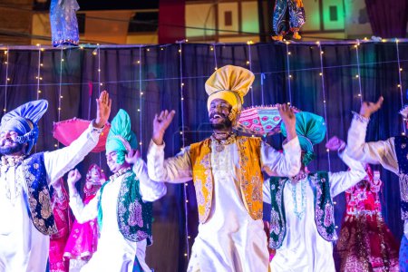 Téléchargez les photos : Bikaner, Rajasthan, Inde - 13 janvier 2023 : Punjabi Bhangra, Groupe de jeunes hommes sikh en robe traditionnelle punjabi colorée et turban exécutant la danse bhangra avec le sourire au festival de chameau. - en image libre de droit