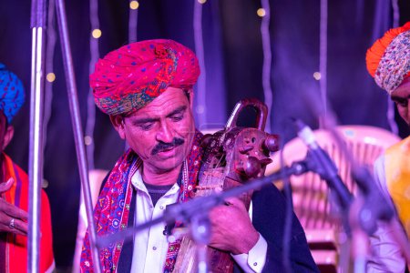 Foto de Bikaner, Rajastán, India - 13 de enero de 2023: Festival de camellos, Retrato de un artista masculino rajastaní actuando en el escenario durante el festival de camellos en bikaner con vestido tradicional rajastaní y turbante colorido. - Imagen libre de derechos