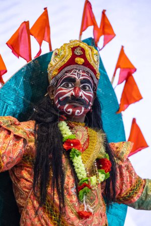 Foto de Nueva Delhi, India - 18 de noviembre de 2023: Retrato de artista folclórico masculino indio con vestido pintado y ropa tribal tradicional en la feria para atraer a los turistas. - Imagen libre de derechos