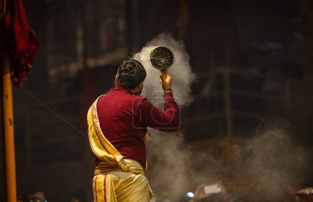 Foto de Varanasi, Uttar Pradesh, India - 18 de enero de 2024: Ganga aarti, Retrato de un joven sacerdote realizando pandillas del río santo aarti vespertino en dashashwamedh ghat con vestimenta tradicional con rituales hindúes. - Imagen libre de derechos