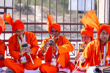 Foto de Faridabad, Haryana, India - February 17 2024: Group of snake charmer artists performing with musical instruments during surajkund craft fair in saffron dress to entertain tourists. - Imagen libre de derechos