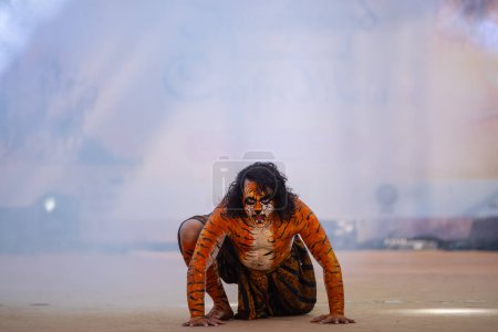 Photo for Faridabad, Haryana, India - February 17 2024: Portrait of an male artist performing classical dance kuchipudi as tiger to save himself from hunter on stage with tiger makeup on his face and body. - Royalty Free Image
