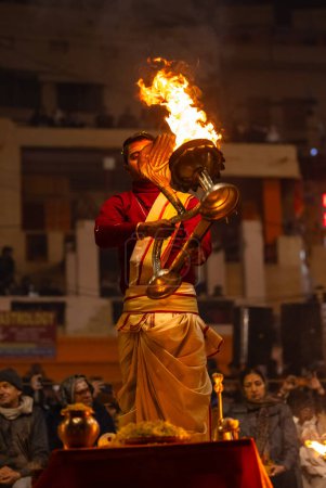 Foto de Varanasi, Uttar Pradesh, India - 18 de enero de 2024: Ganga aarti, Retrato de un joven sacerdote que realiza un aarti nocturno en el río sagrado Ganges en Dashashwamedh Ghat con vestimenta tradicional y rituales hindúes. - Imagen libre de derechos