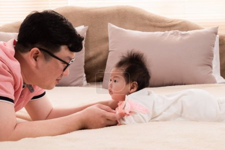 Photo for Selective focus father and healthy newborn 3 months baby eye contact together on bed, happy dad spent time talk to daughter at home. toddler infant prone by herself look to dad lift head up. - Royalty Free Image