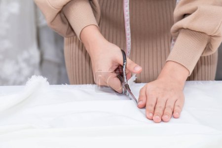 Photo for Selective focus of hand working woman cutting fabric with scissors while sewing custom made clothes and design wedding dress in work shop. Fashion designer work at creative office. - Royalty Free Image