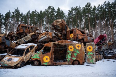 Foto de 03.02.2023 Irpin, Ucrania: Apilado un montón de coches estrellados después de los ataques de fuego y misiles en la ciudad con el arte en ellos. Pintura de girasol en los coches destruidos - Imagen libre de derechos