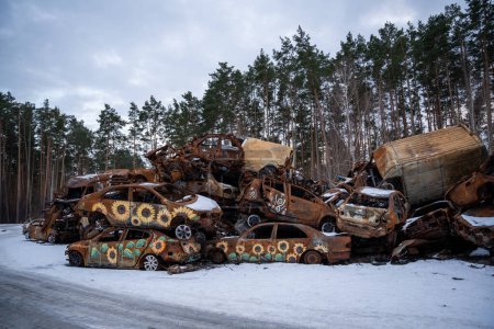 Foto de 03.02.2023 Irpin, Ucrania: Apilado un montón de coches estrellados después de los ataques de fuego y misiles en la ciudad con el arte en ellos. Pintura de girasol en los coches destruidos - Imagen libre de derechos