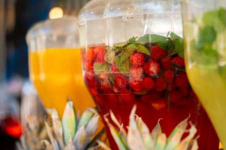 Foto de Una serie de coloridos dispensadores de agua infundidos en frutas, flanqueados por piñas y cocos, creando una escena de refresco tropical - Imagen libre de derechos
