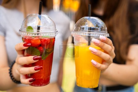 Close-up of women's hands holding vibrant fruit tea cocktails with fresh strawberries and lemon slices, reflecting a sociable summer vibe.