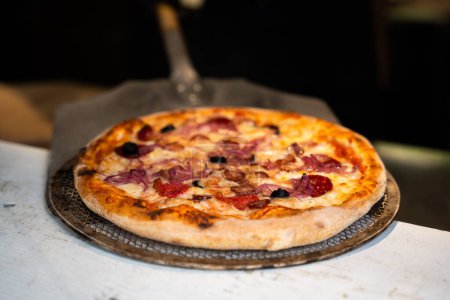 Foto de Primer plano de una pizza artesanal recién horneada con el interior del chef y el restaurante en el fondo, fuera de foco - Imagen libre de derechos