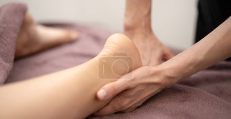 Téléchargez les photos : Les mains habiles d'un masseur offrent un massage des tissus profonds sur la jambe d'un client, offrant un soulagement de l'oppression musculaire dans un cadre de spa tranquille. - en image libre de droit