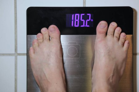 Stainless steel digital scale with mans feet weighing 185 pounds on tile floor