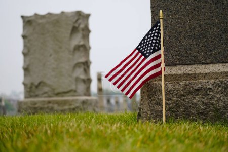 Photo for Closeup on American flag places my cemetery gravestone on grey cloudy day with selective focus - Royalty Free Image