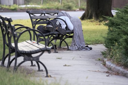 Anonymous homeless man and possible drug addicts sleeping on a New York City park bench with blanket over head