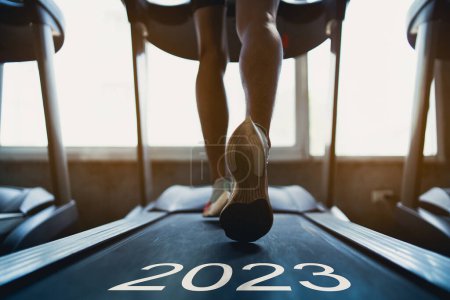Ein frohes neues Jahr 2023.2023 symbolisiert den Beginn des neuen Jahres. Füße aus nächster Nähe, Läufer auf dem Laufband im Fitnessclub. Ausdauertraining. Gesunder Lebensstil, Kerlentraining im Fitnessstudio.