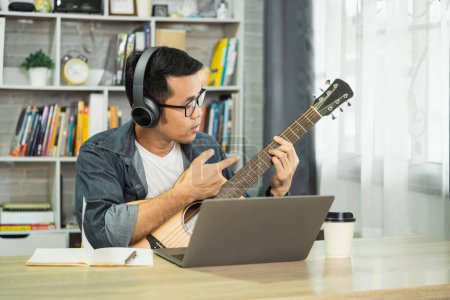 Téléchargez les photos : Des musiciens asiatiques portant un casque et apprenant la guitare en ligne via vidéo, maîtrisant les compétences, tout en enseignant aux étudiants avec passion, créativité grâce à des leçons virtuelles. Concept d'éducation musicale. - en image libre de droit