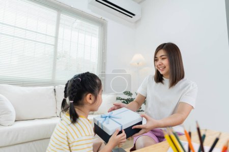 Photo for Grateful asian girl holding blue present box giving mothers day gift to mom. Happy mom and cute daughter kid child celebrating birthday, hugging on couch sofa at home. Happy family concept. - Royalty Free Image