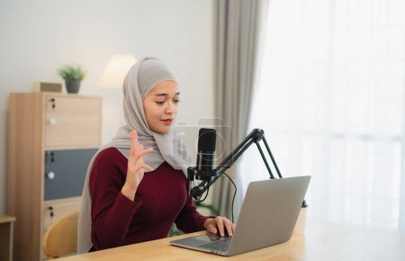 Muslim Islam freelance entrepreneur woman wearing hijab and talking while conference meeting, working using microphone and laptop and on desk table at the home office. Business conference technology.